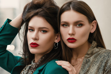 Close up portrait of two young beautiful fashionable women with red lips makeup, wearing trendy...
