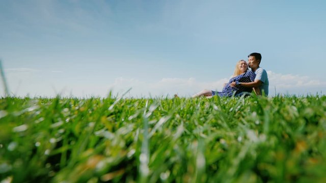 Asian man with a pregnant woman are resting in nature in a picturesque place, sit on the green grass