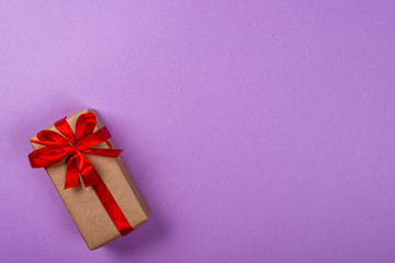 Gift box with bow over purple neon background. Space for text on the right side of the image.