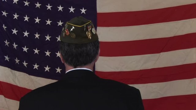 A man in a VFW cap walking up to and old faded 48 star American flag and saluting