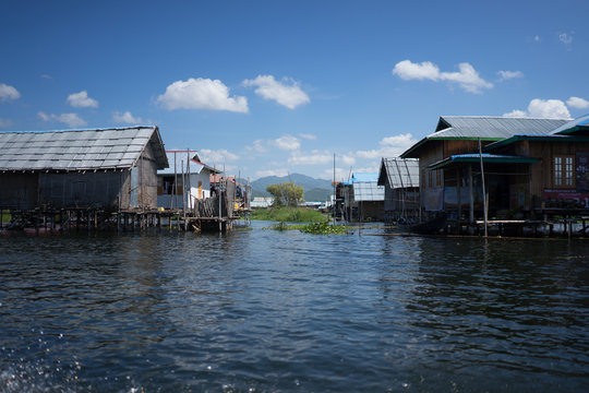 Pływająca wioska na Inle Lake na tle g&oacute;r z wystającymi słupami elektrycznymi.