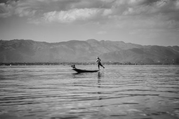 Sylwetka rybaka z Inle Lake łowiącego ryby z łodzi na jeziorze na tle gór - czarno białe. - obrazy, fototapety, plakaty