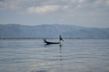 Sylwetka rybaka z Inle Lake łowiącego ryby z łodzi na jeziorze na tle gór.