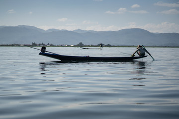 Rybak z Inle Lake łowi ryby na jeziorze z drugą łodzią w tle.