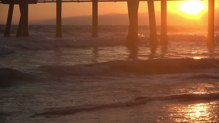 Sunset reflecting on the ocean waves under a pier in slow motion