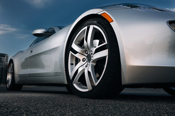 Obraz na płótnie Canvas Modern luxury supercar front wheel rims. Silhouette of modern silver sportcar at the empty parking 