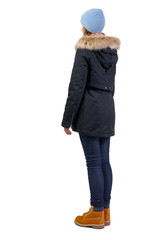 Side view woman in a black winter jacket with fur and blue hat.