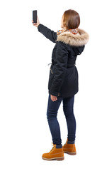 Back view woman in winter jacket who makes selfie with a smartphone.