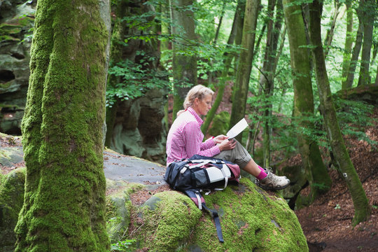 Germany, Rhineland-Palatinate, Eifel Region, South Eifel Nature Park, View of woman hiker sitting on bunter rock formations at beech tree forest