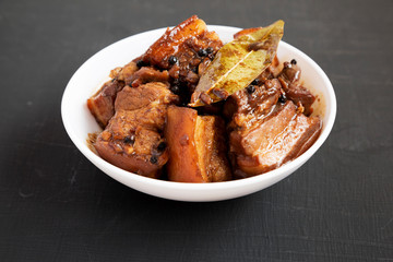 Homemade Filipino Adobo Pork in a white bowl on a black background, side view. Close-up.