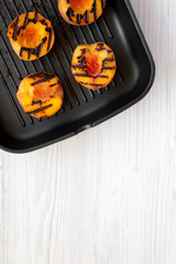 Homemade grilled peaches in a grilling pan on a white wooden surface, top view. Flat lay, overhead, from above. Space for text.