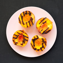 Overhead view, homemade grilled peaches on a pink plate on a black surface. Flat lay, top view, from above. Close-up.