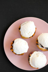 Homemade grilled peaches with vanilla ice cream on a pink plate on a black background, top view. Flat lay, overhead.