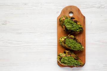 Grilled chimichurri chicken breast on a rustic wooden board on a white wooden surface, top view. Space for text.