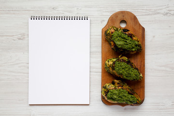 Grilled chimichurri chicken breast on a rustic wooden board, blank notepad on a white wooden background, top view. Copy space.