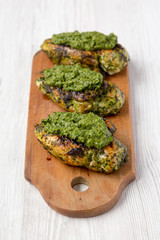 Grilled chimichurri chicken breast on a rustic wooden board on a white wooden surface, low angle view.