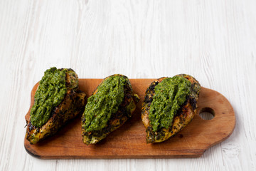 Grilled chimichurri chicken breast on a rustic wooden board on a white wooden background, side view. Copy space.
