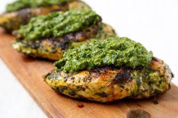 Grilled chimichurri chicken breast on a rustic wooden board on a white wooden background, side view. Close-up.