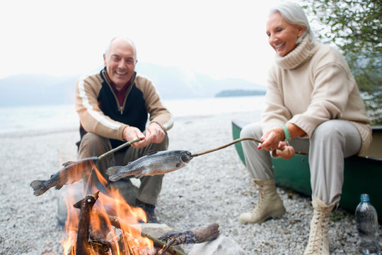 Senior couple grilling fish at campfire