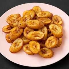 Homemade fried plantains on a pink plate on a black background, side view. Close-up.