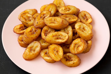 Homemade fried plantains on a pink plate on a black backgound, low angle view. Closeup.