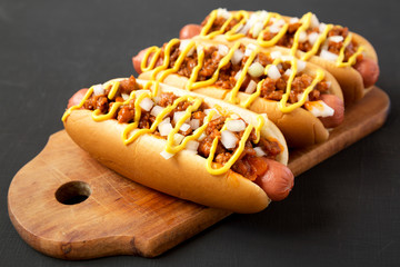 Homemade Detroit style chili dog on a rustic wooden board on a black background, side view. Closeup.