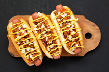 Homemade Detroit style chili dog on a rustic wooden board on a black background, top view. Closeup.
