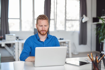 Fototapeta premium Young Caucasian employee sitting in office and typing on laptop. Start up business concept.