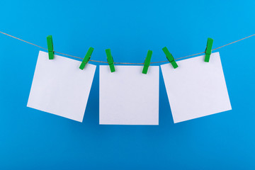 white sheets of notepad for notes and reminders, fastened with decorative green clothespins, hang on a rope on a blue background