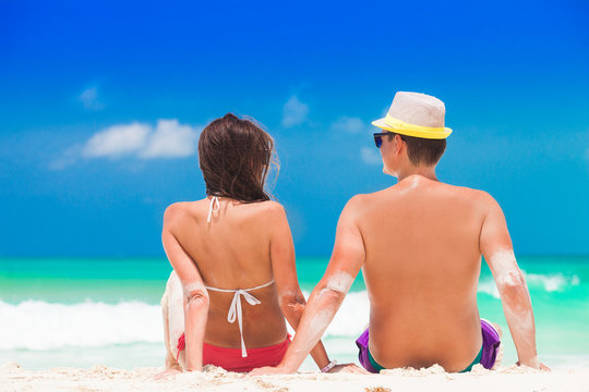 Back view of a man and woman couple sitting on caribbean white sand beach
