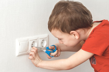Little boy plays with electric socket and scissors. High voltage hazard