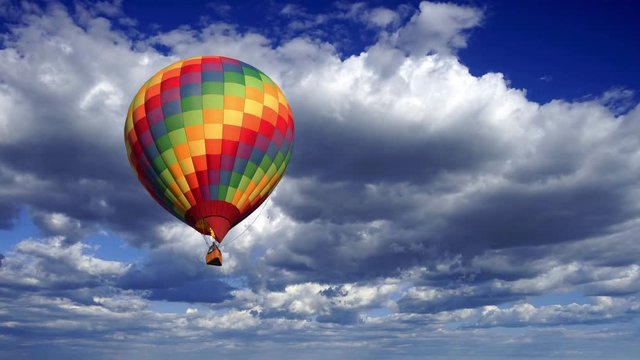 A colorful hot air balloon coming closer against a fluffy clouds time lapse sky.
