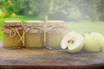 Sugar free apple puree jars on the wooden table in blurred garden background. Freshly prepared organic homemade baby food.