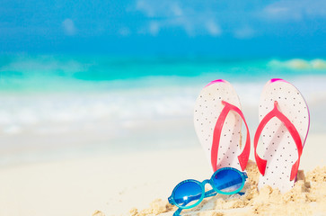 Straw hat, bag, sun glasses and flip flops on a tropical beach
