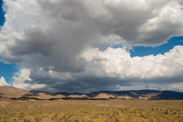 gray and white rain clouds cast shadows over vast desert hills California