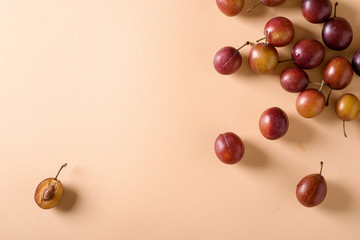 Scattered sliced half ripe sweet plum fruits with water drops on cream colored background, bright, top view, flat lay, copy space