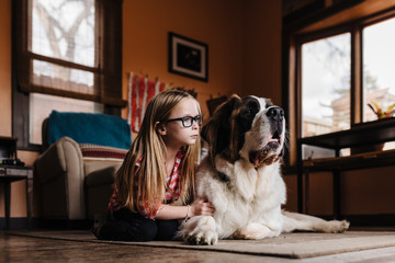 Girl with St. Bernard dog sitting on rug at home