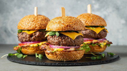 A set of homemade delicious burgers of beef, bacon, cheese, lettuce and tomatoes on a light concrete background. Fat unhealthy food close-up