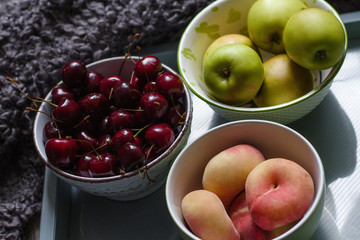 Composition with cherries, apples and peaches on a tray with a plaid in the background