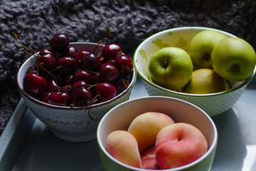 Composition with cherries, apples and peaches on a tray with a plaid in the background