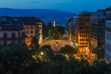 Dusk view of Geneva city streets with buildings, Geneva Lake (Lac Leman) and lighthouse during beautiful summer night, Geneva, Switzerland