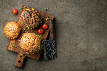 Tasty grilled home made burger with beef, tomato, cheese, bacon and lettuce on a dark stone background with copy space. Top view. fast food and junk food concept. Flat lay