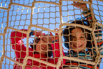 Laughing girls looking through rope net against blue sky