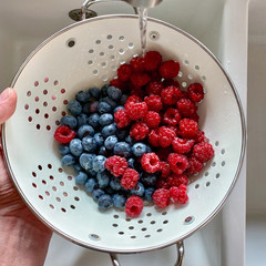 Men Hand washing raspberry and blueberry in a large metal bowl with water on the Kitchen Sink. Top view