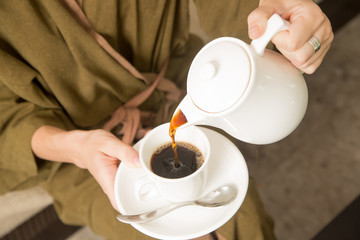 Woman pouring coffee from the kettle into the cup