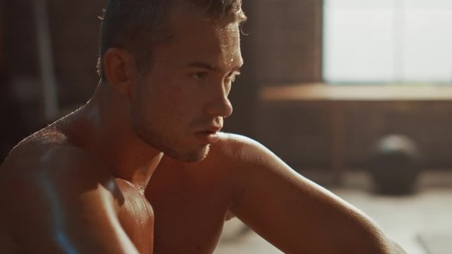 Strong Handsome Fit Shirtless Man Sitting in a Loft Industrial Gym with Motivational Posters. He's Catching His Breath after Intense Fitness Training Workout. Sweat All Over His Body.