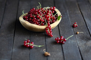 red currant in wooden plate on dark wooden background.