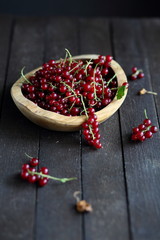 red currant in wooden plate on dark wooden background.
