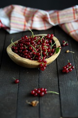 red currant in wooden plate on dark wooden background.