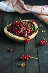 red currant in wooden plate on dark wooden background.
